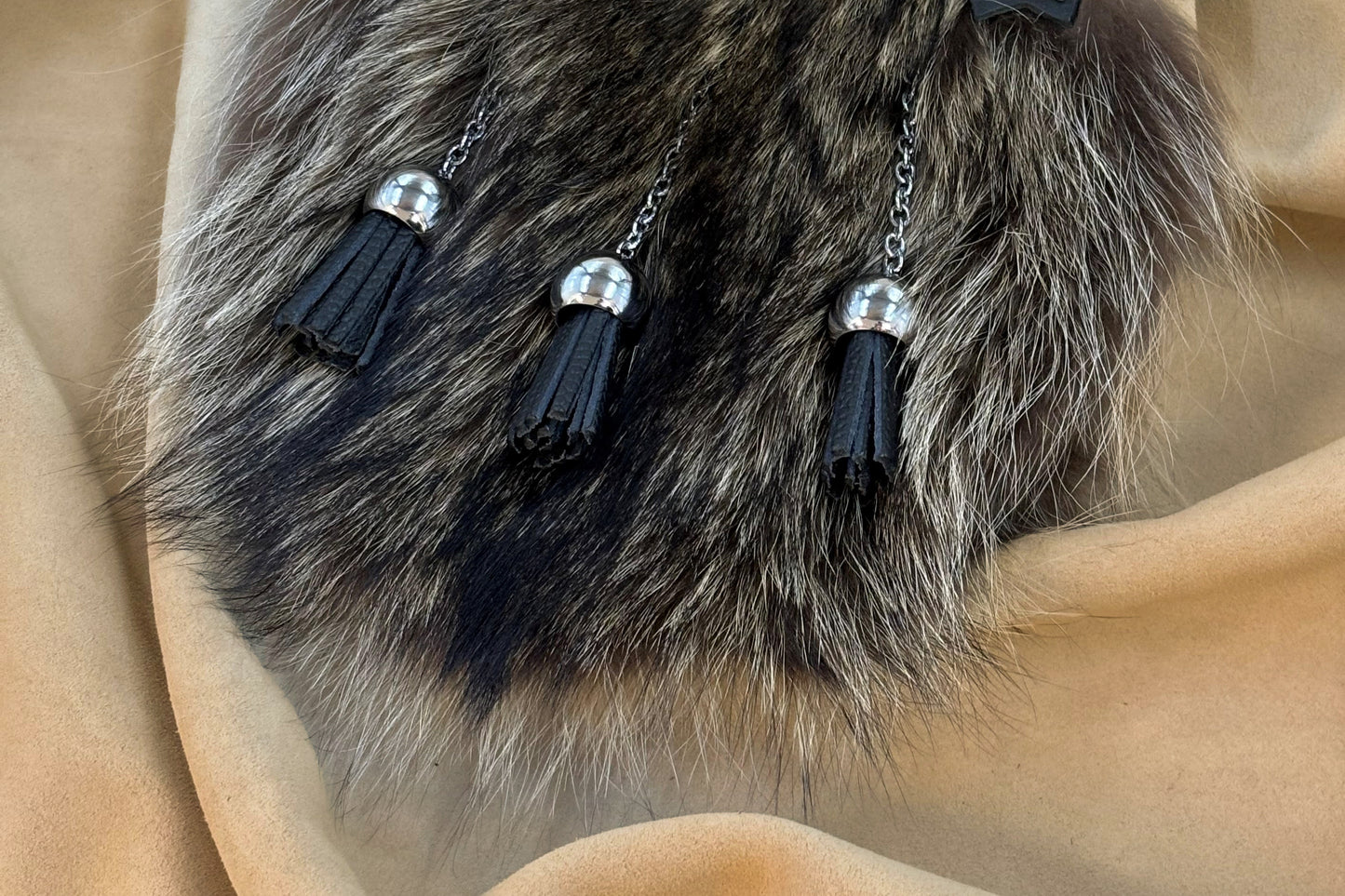 Close up of 3 black leather tassels mounted on silver chains and ball bells.